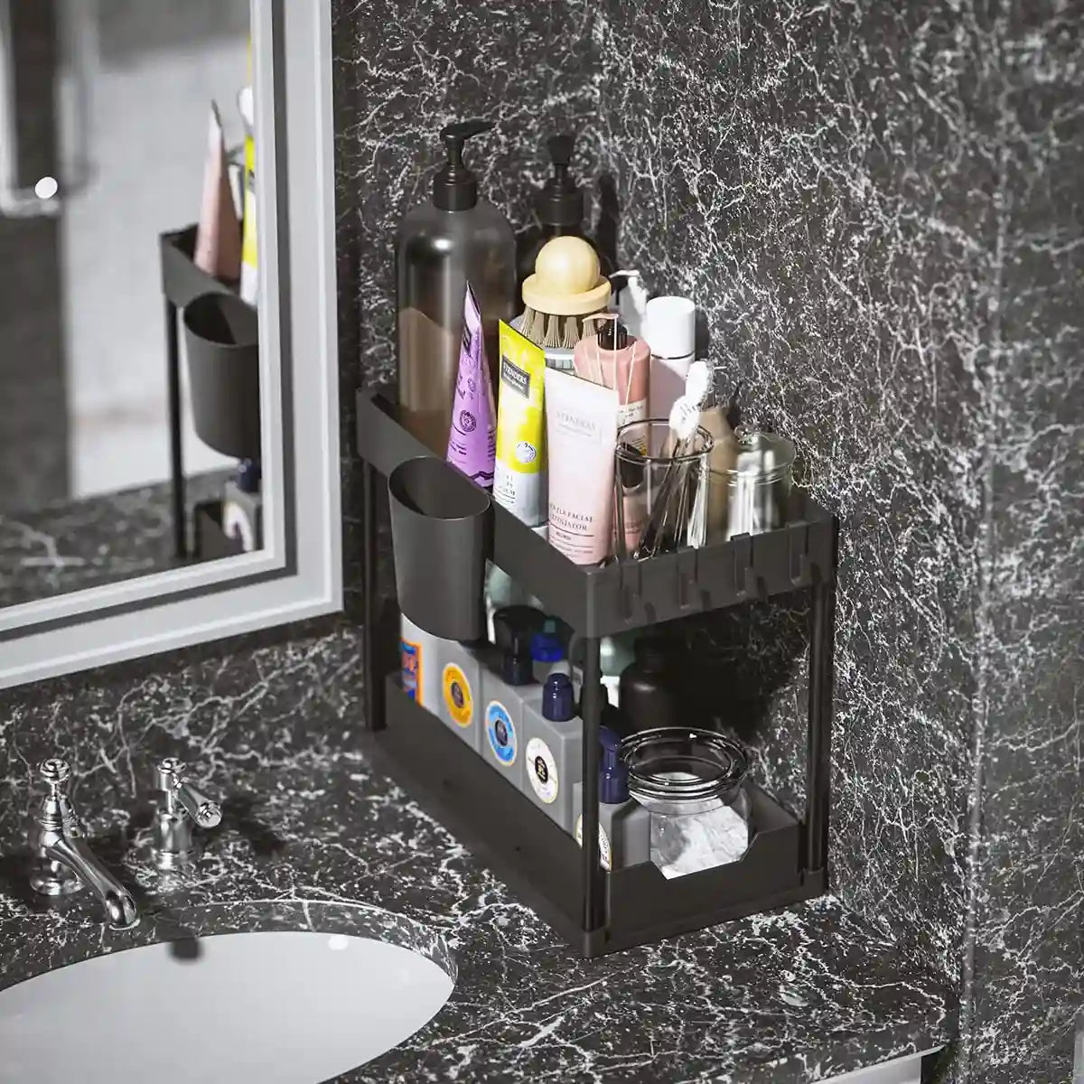 Bathroom counter with a black multi-tiered organizer holding various toiletries against a marble wall.