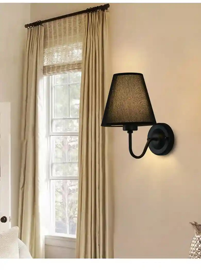 Black wall sconce lamp on a beige wall with curtains in the background