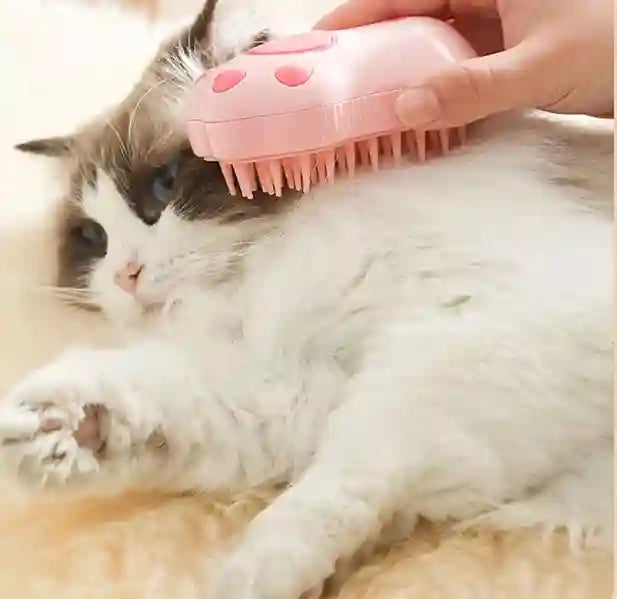 Cat being groomed with a pink grooming brush on a soft surface