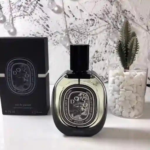 Diptyque perfume bottle and packaging on a white surface with decorative elements.
