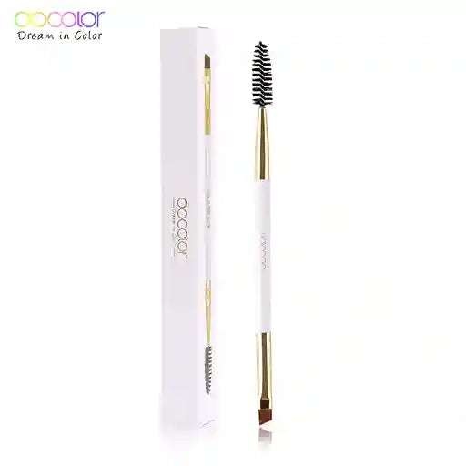 Eyebrow brush with gold handle and black bristles next to its packaging on a white background