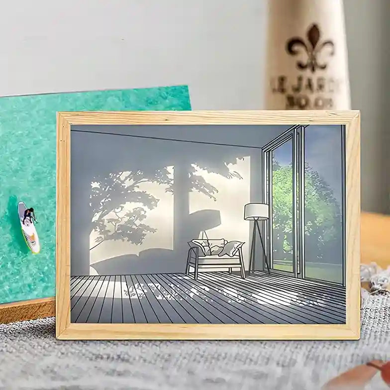 Framed artwork of a room with a large window and outdoor view, placed on a surface.