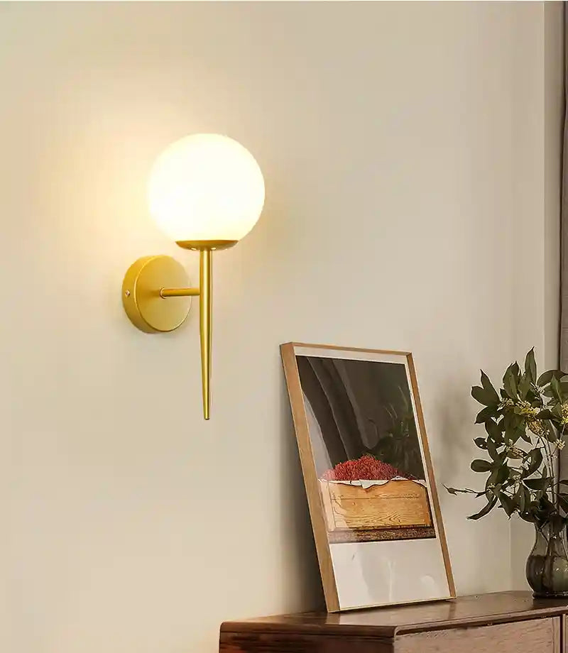 Gold wall sconce on a wall with a framed picture and plant in the background