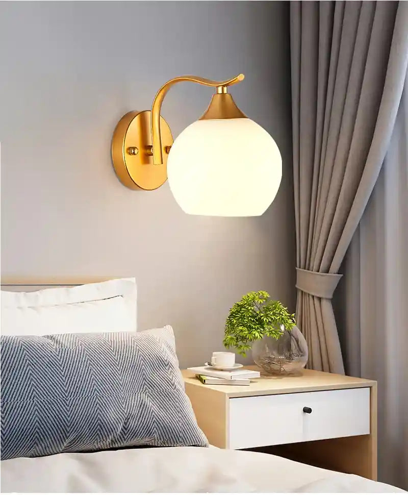 Gold wall sconce with a white glass shade in a bedroom setting.