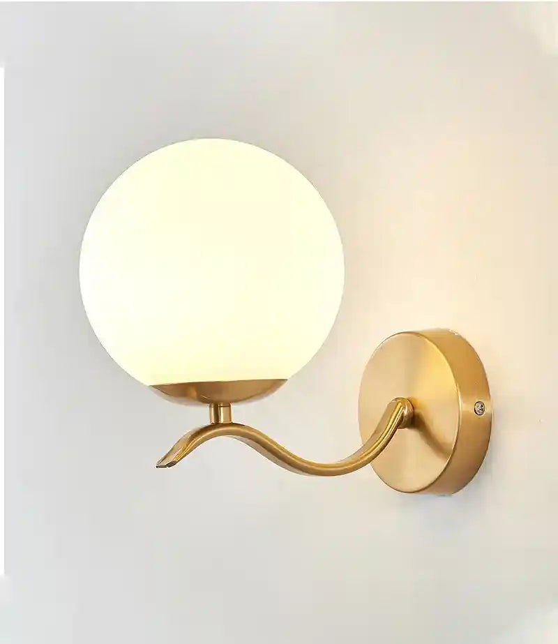 Gold wall sconce with a white globe light on a plain background