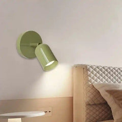 Green wall lamp on a white wall next to a bed with a quilted headboard.