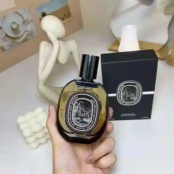 Hand holding a Diptyque perfume bottle with its packaging on a neutral background