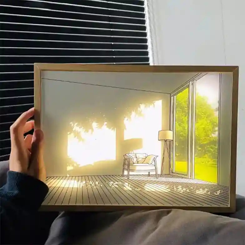 Hand holding a framed picture of a sunlit room with a chair and window.