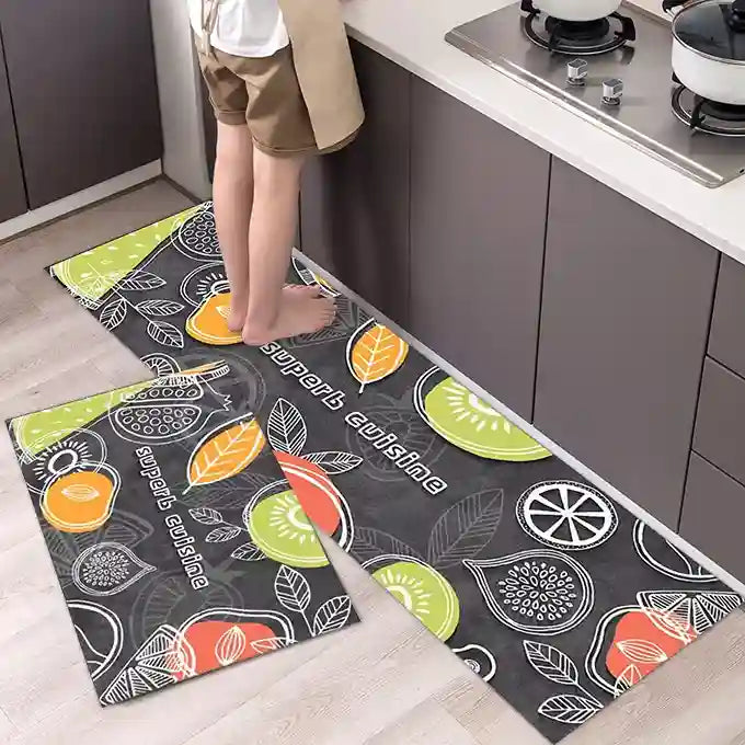 Kitchen floor with patterned mats featuring fruits and text, person stepping onto one of them.