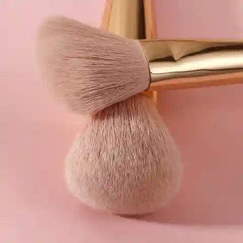 Makeup brush with gold handle on a pink background