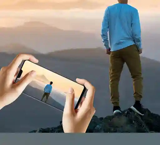 Person taking a photo of another person standing on a mountain with a phone.