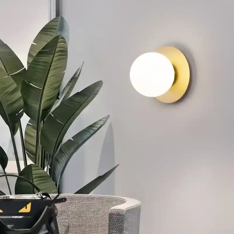 Round wall light fixture on a gray wall with a plant and chair in the foreground
