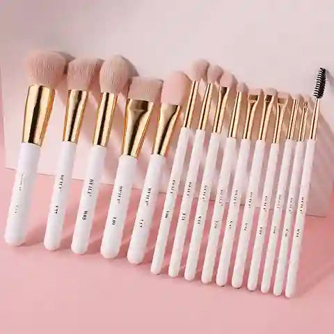 Set of makeup brushes with gold and white handles on a pink background