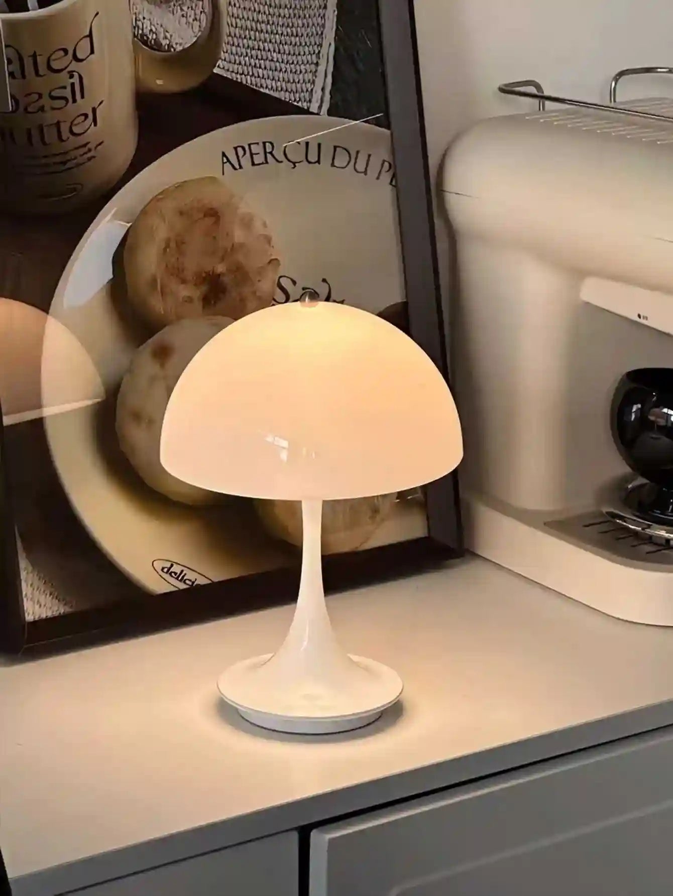 Small white lamp on a kitchen counter with a coffee machine and plates in the background.