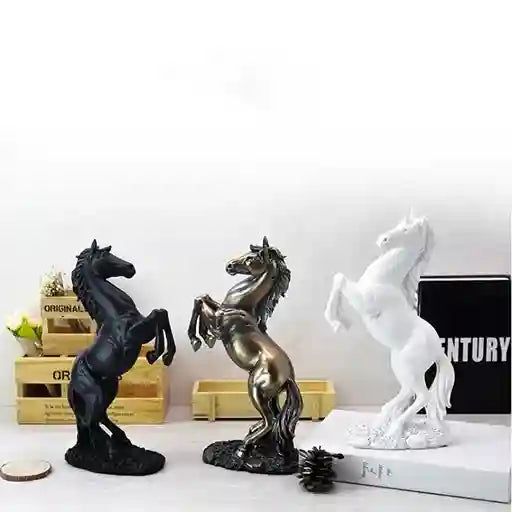 Three horse statues in black, bronze, and white on a white surface with a blurred background.
