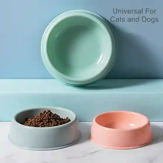 Three pet bowls in green, gray, and pink on a marble surface with a light blue background.