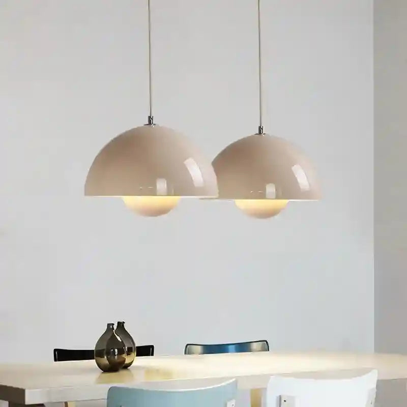Two beige pendant lights hanging above a dining table with a vase and chairs in the background.
