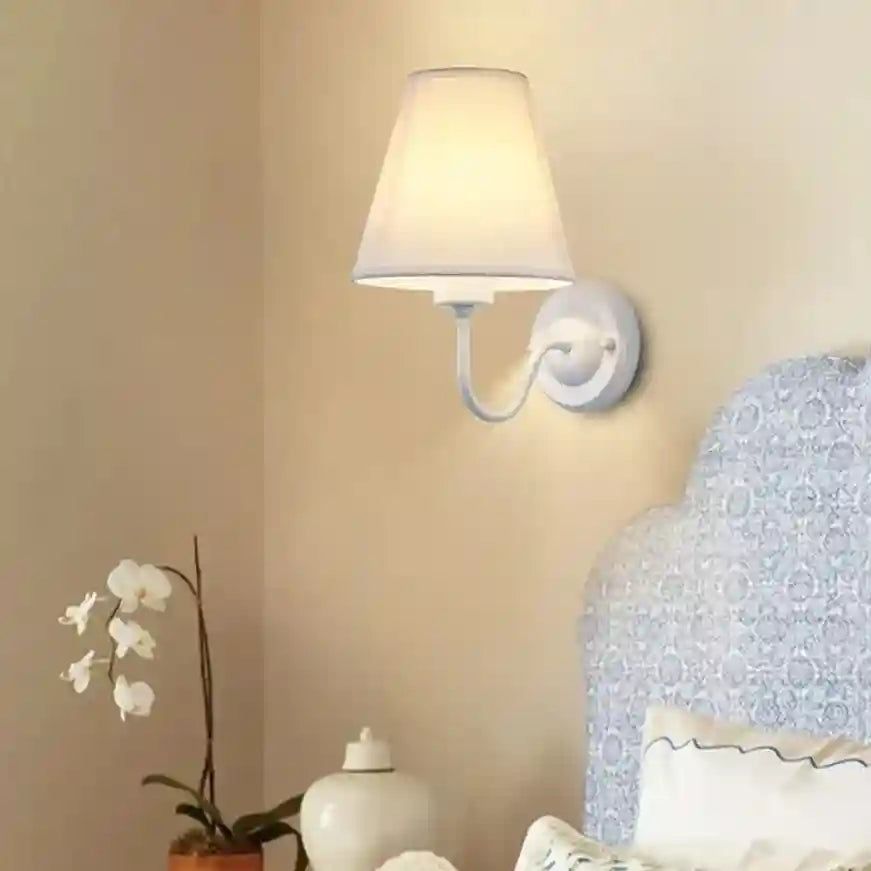 Wall-mounted lamp with a beige shade on a beige wall, next to a decorative vase and plant.