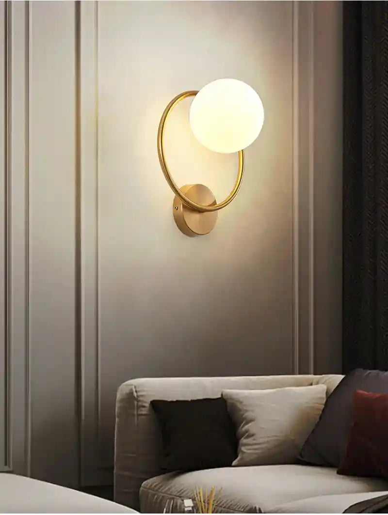Wall-mounted lamp with a round glass shade on a neutral wall above a sofa.
