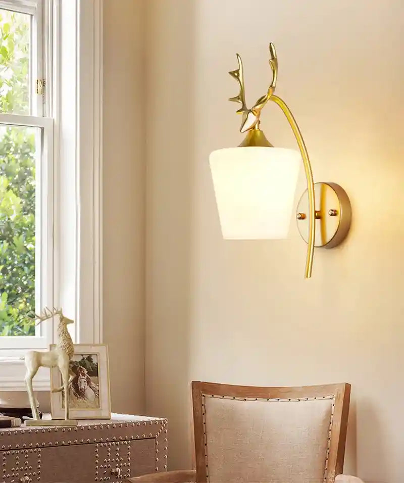 Wall-mounted lamp with gold finish and glass shade in a room with a window and decorative items.