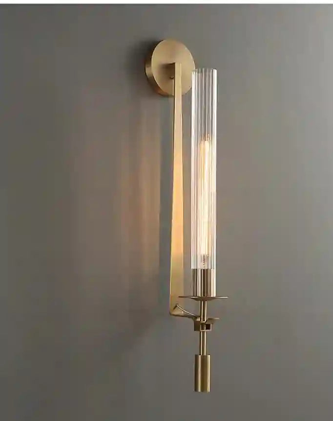 Wall-mounted lamp with gold fixture and clear glass shade on a gray wall