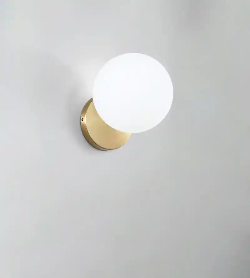 Wall-mounted light fixture with a gold base and white globe on a gray background