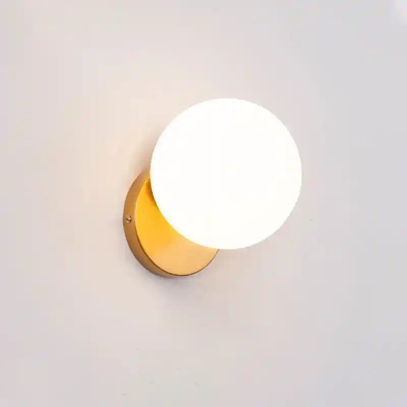 Wall-mounted light fixture with a white globe and gold base on a light gray background
