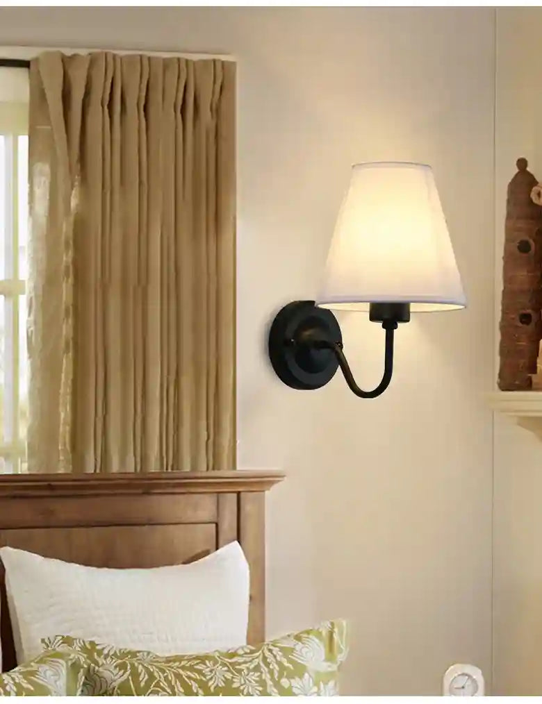Walls lamp on a white wall with a wooden headboard and pillows.