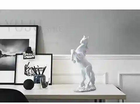 White horse statue on a table with framed pictures in the background